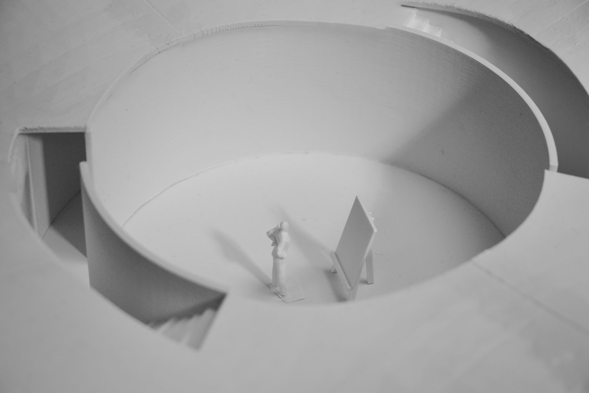 Model seen from above: a circular room cut into the plan, with a small figure and an easel standing in it and steps leading in at the edge.