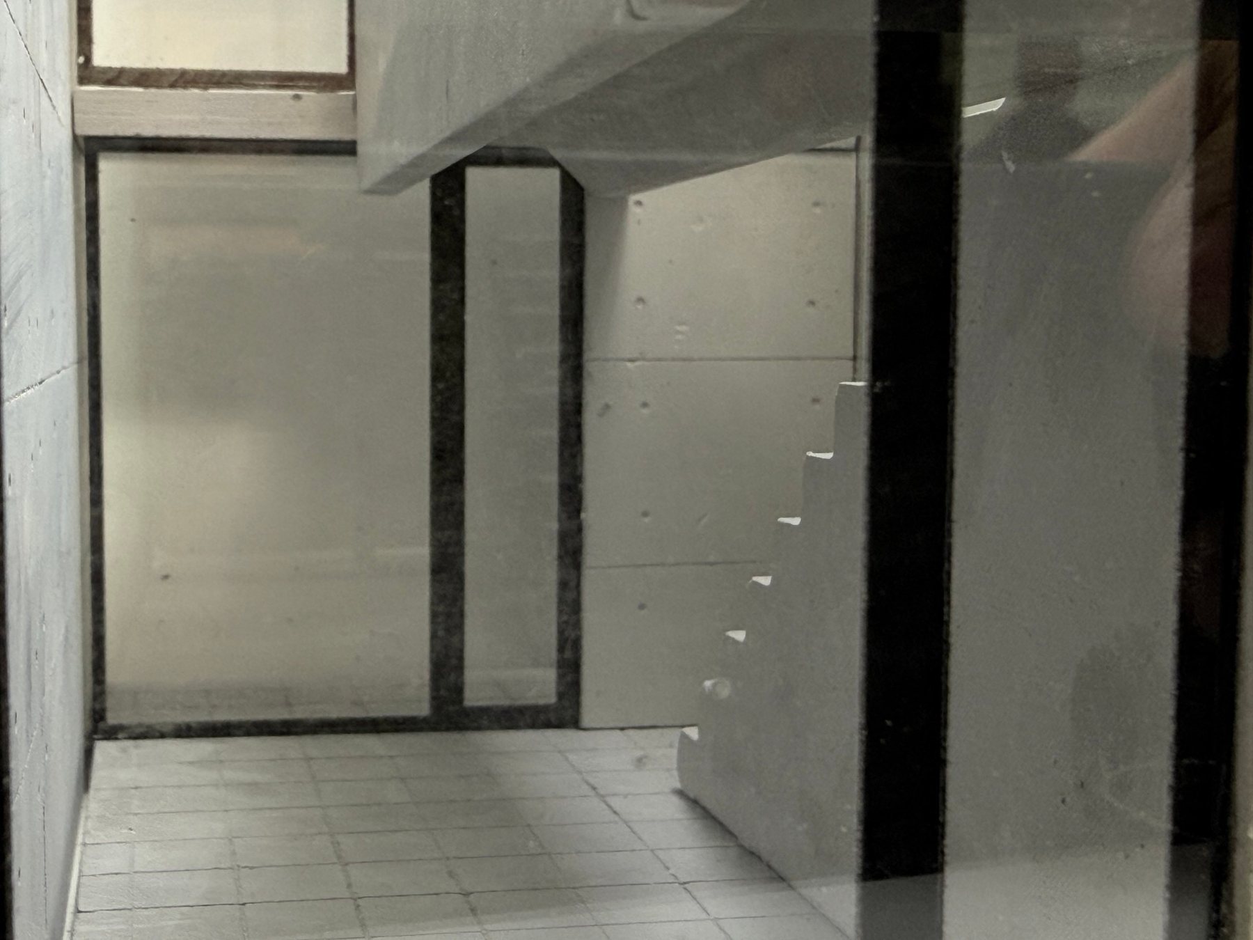 Interior detail of the model: a stair beside a glazing frame, a tiled floor and a wall with tie holes.
