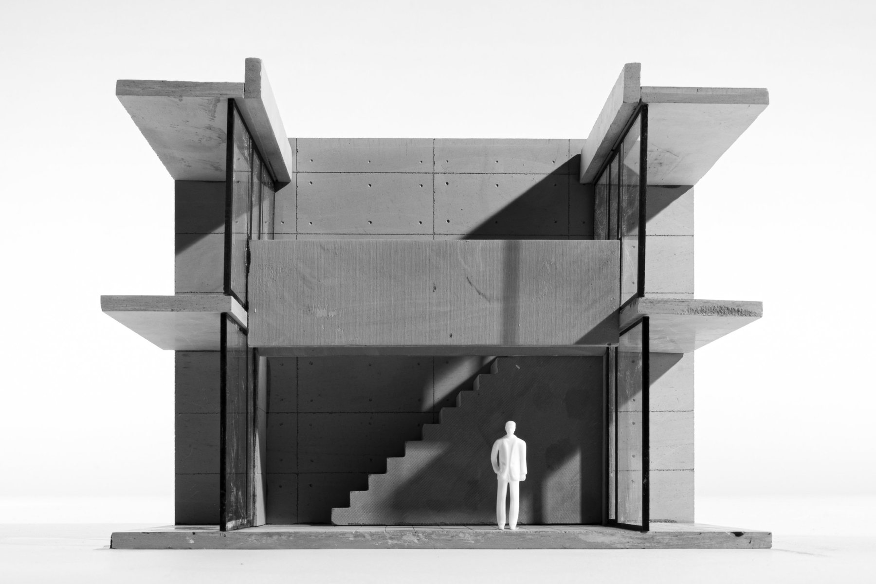 Front view of a grey model of a two-storey house open to the viewer, with a small white figure standing by a stair.
