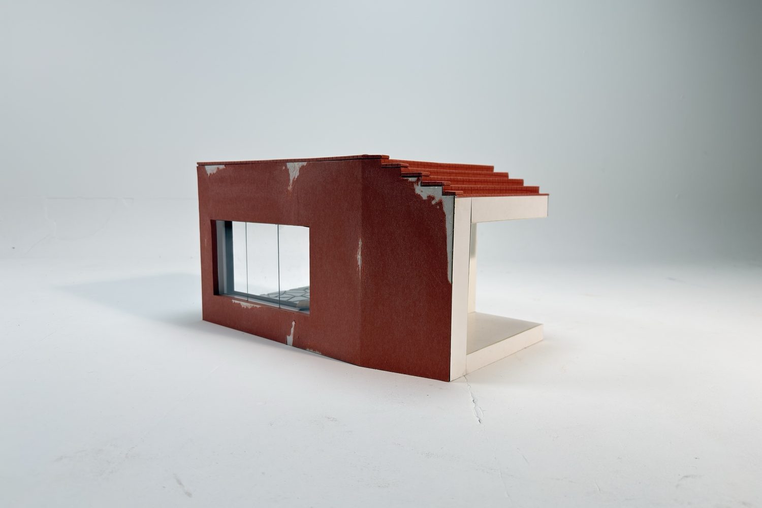 Side view of the model: terracotta wall, a stepped roof of red tiles and an open white porch.