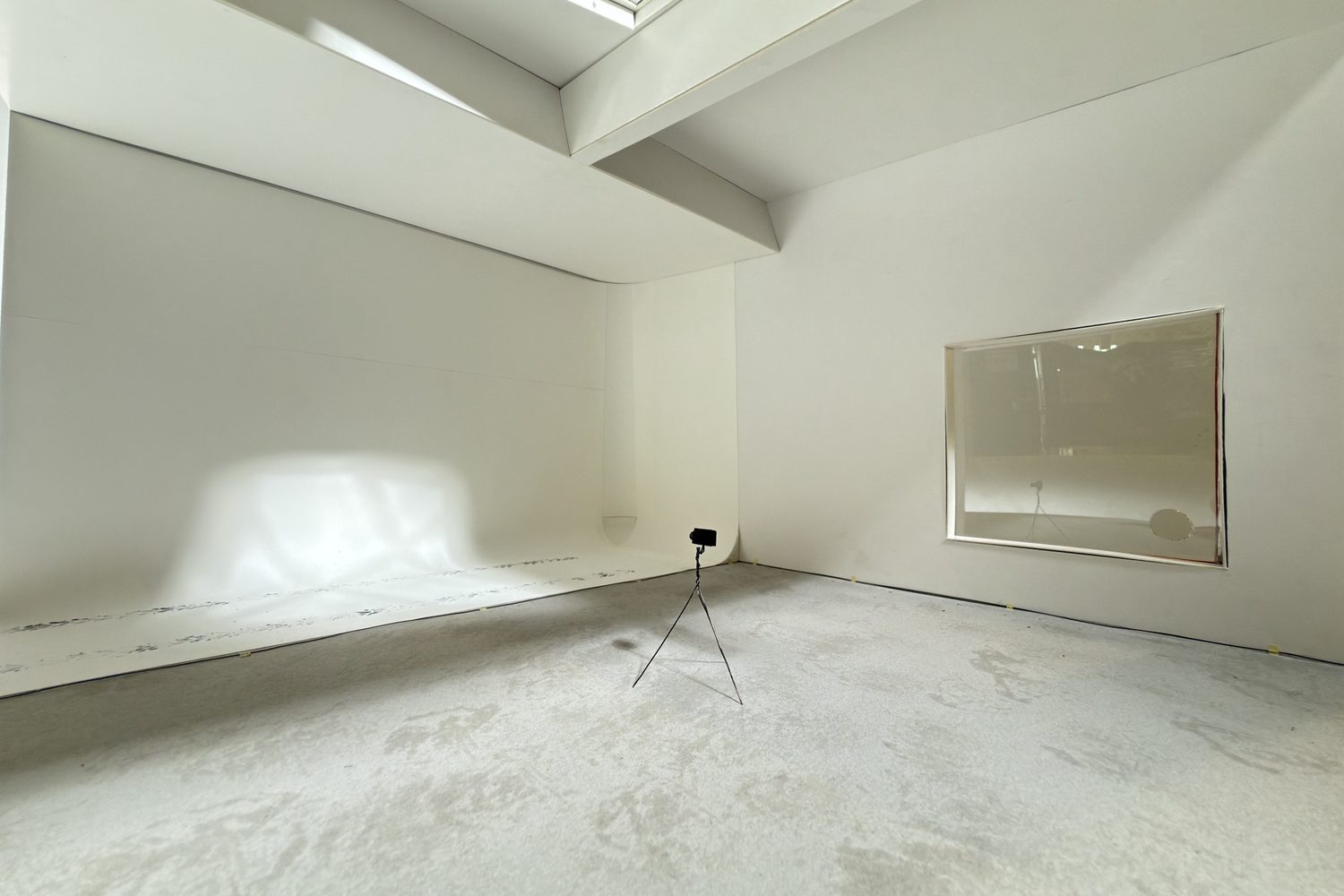 Interior of a white model room with a skylight, a curved wall meeting the floor, a window and a camera on a tripod.