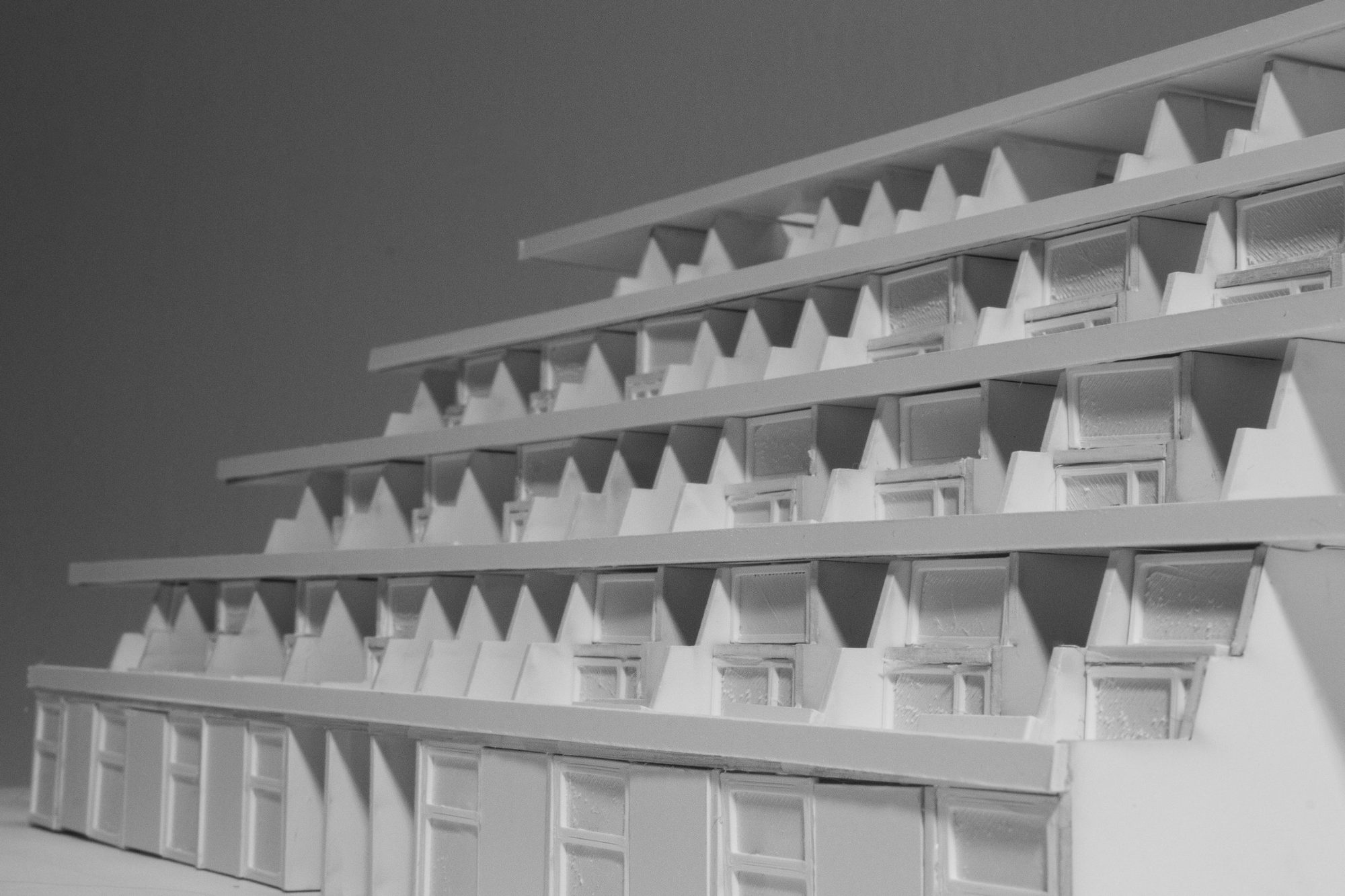 Close-up of the model facade: triangular supports, deep terraces and windows in white card.