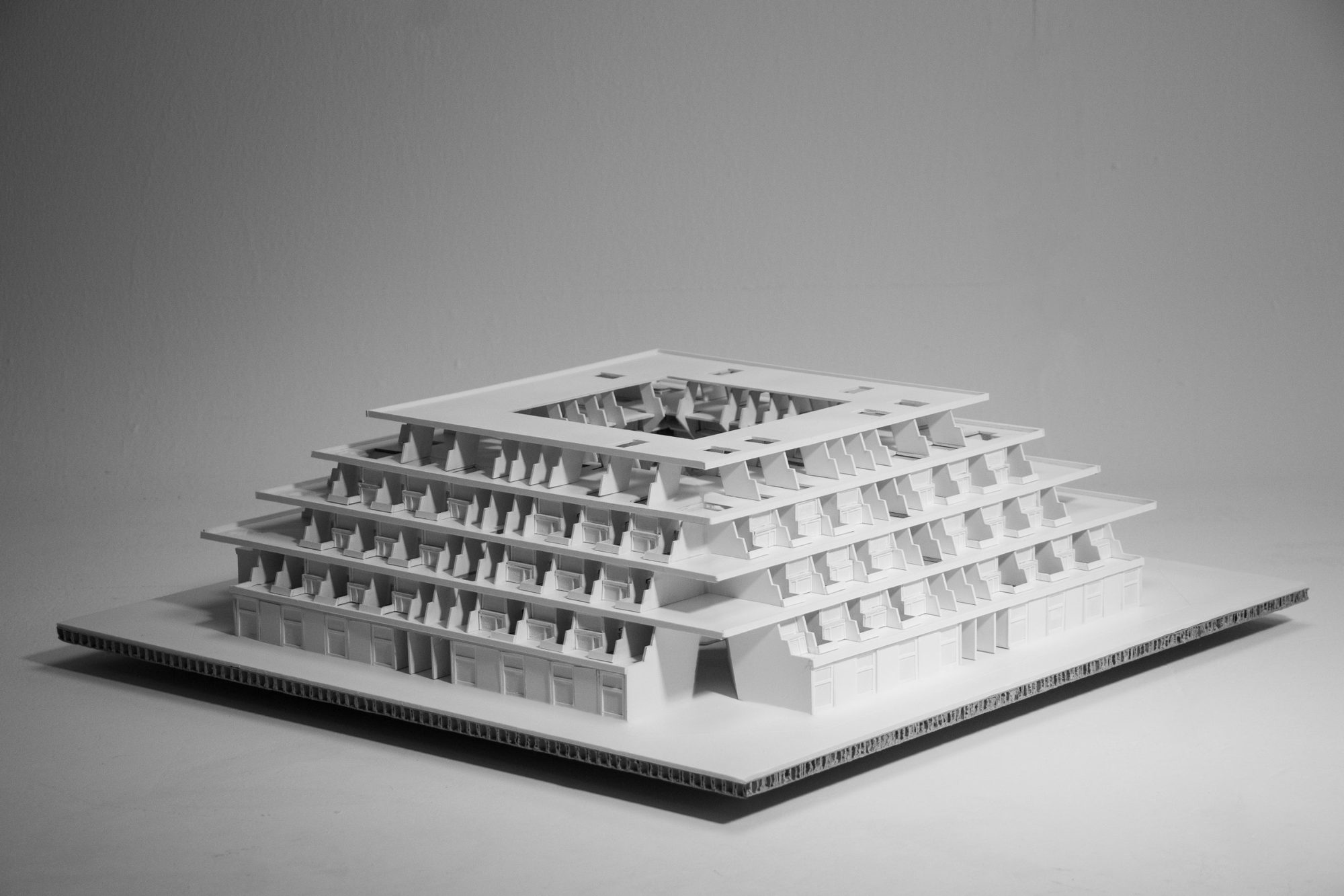 White card model of the stepped block on a honeycomb board, photographed against a grey backdrop.