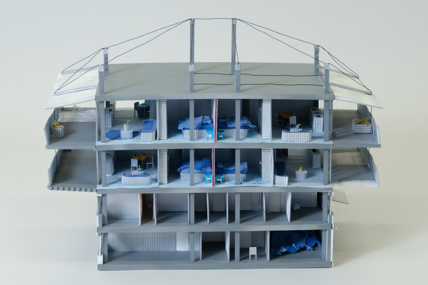 Front of the model, cut open: two living storeys with beds and furniture above two open floors, and roof posts with cables.