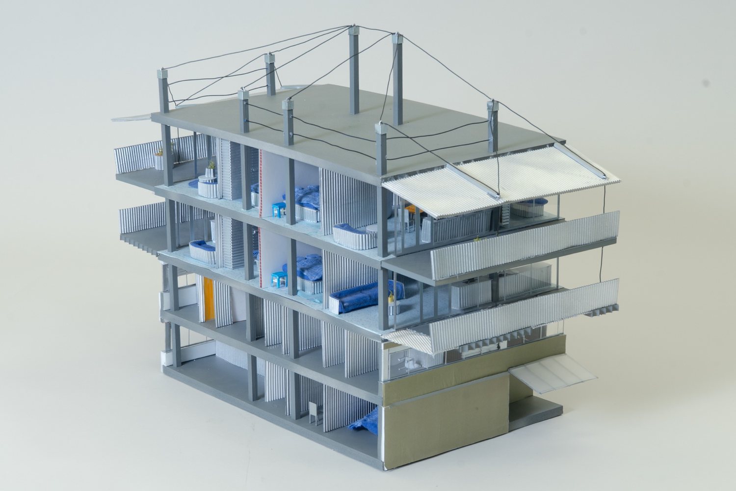 Model seen from the opposite corner, with open floors below the living levels and an olive-coloured volume with a canopy at the lower right.