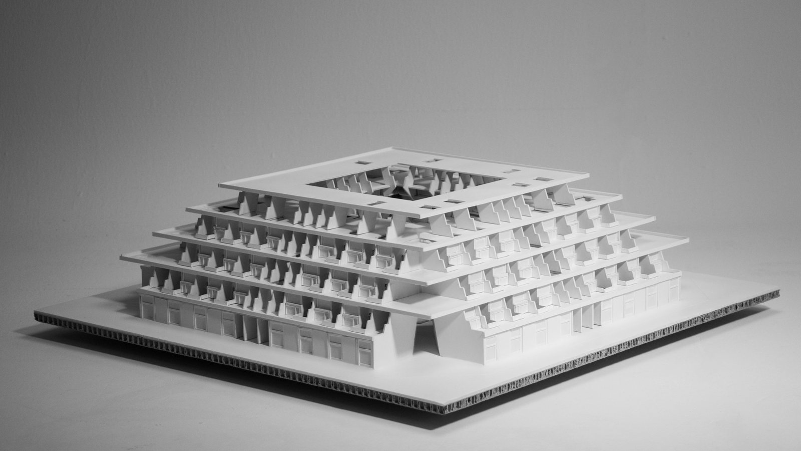 White card model of the stepped apartment block on a honeycomb board, with a square opening at the top and terraces stepping down on all sides.